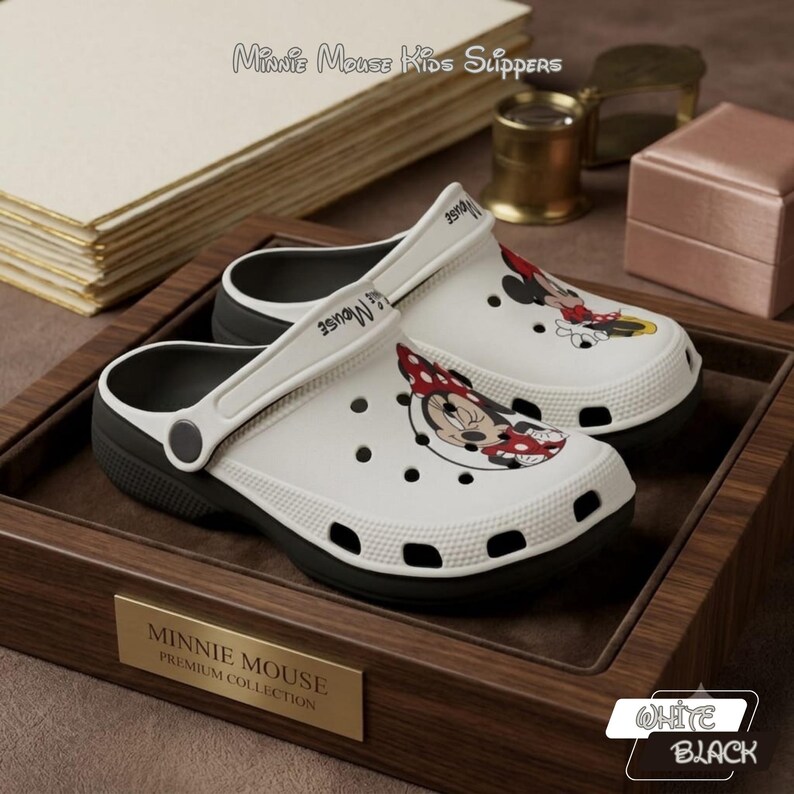 K&ouml;nnte beinhalten: Wei&szlig;e und schwarze Minnie Mouse Kinderslipper. Die Slipper zeigen eine Minnie Mouse Grafik auf der Vorderseite und den Text "Minnie Mouse Kids Slippers". Die Slipper befinden sich in einem Holztablett mit einer goldenen Plakette mit der Aufschrift "Minnie Mouse Premium Collection".
