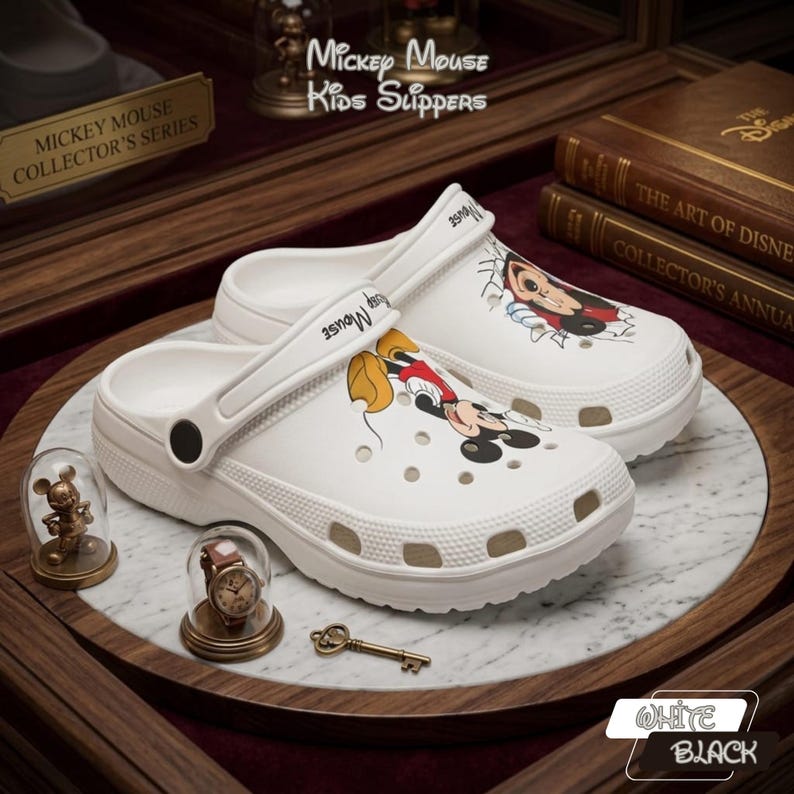 K&ouml;nnte beinhalten: Wei&szlig;e Mickey Mouse Kinder-Hausschuhe mit Mickey Mouse-Grafiken. Die Hausschuhe geh&ouml;ren zur Mickey Mouse Collector's Series. Das Bild enth&auml;lt auch dekorative Elemente und den Text "Mickey Mouse Kids Slippers."