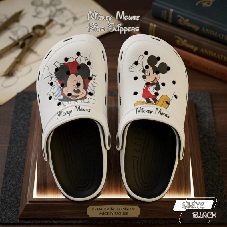 K&ouml;nnte beinhalten: Wei&szlig;e Mickey Mouse Kinder-Hausschuhe mit schwarzen Sohlen. Jeder Hausschuh zeigt eine andere Mickey Mouse Grafik. Der Text "Mickey Mouse Kids Slippers" ist sichtbar. Die Hausschuhe werden auf einem Holzst&auml;nder pr&auml;sentiert.