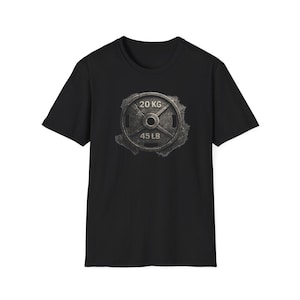 May include: Black t-shirt with a distressed graphic of a weight plate. The design includes the text "20 KG" and "45 LB". The shirt has a crew neck.