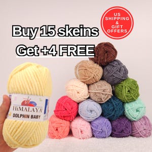 May include: A collection of colorful Himalaya Dolphin Baby yarn skeins. The image features a large yellow skein held by a hand, and a pyramid of various colored skeins, including pink, blue, green, and brown. Text reads "Buy 15 skeins Get +4 FREE".