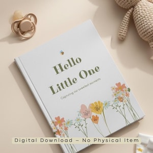 May include: A white baby memory book with the text "Hello Little One" and floral illustrations. A pacifier and a crocheted stuffed animal are also in the image. The book's subtitle reads "Capturing our sweetest moments."