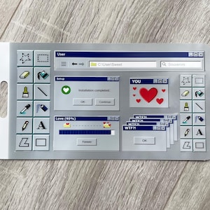 Peut inclure: Un autocollant argenté avec un design d'interface informatique rétro. Il présente des icônes, des fenêtres avec du texte comme "YOU" et "Love (95%)", et une barre de recherche. L'autocollant a un trou pour l'accrocher.