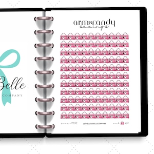 Peut inclure: Un planificateur avec une couverture noire et une reliure argentée, avec le logo "Lula Belle" et un nœud bleu sarcelle. La page de droite affiche une grille d'illustrations de sacs à main roses intitulée "arm candy savings."