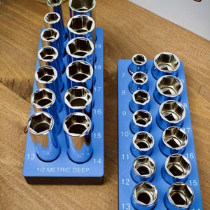 May include: Two blue socket organizers with chrome sockets. The left organizer is labeled "1/2 METRIC DEEP" and the right is labeled "1/2 METRIC SHALLOW". The sockets are numbered from 7 to 19. The image also shows a "TOOL STORAGE" sign.