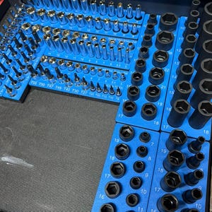 May include: Organized set of sockets and bits in a blue tool organizer. The sockets are various sizes and shapes, including hex and star patterns. The tools are arranged neatly, ready for use in a workshop or garage.