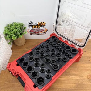 Op de afbeelding: Een rode Milwaukee Packout-organizerkoffer met een zwart schuimrubberen inzetstuk met talloze zeskantige doppen van verschillende groottes. De doppen zijn in rijen gerangschikt met gedrukte labels voor afmetingen in inches en millimeters.