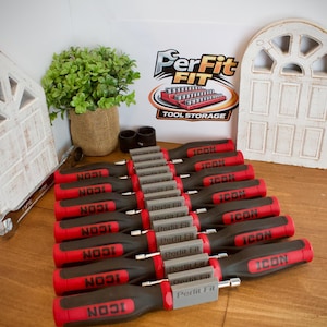 Puede incluir: Un conjunto de destornilladores negros y rojos con el logotipo "ICON", dispuestos sobre una superficie de madera. Los destornilladores están organizados con soportes grises. La imagen también incluye recortes decorativos de madera y un letrero que dice "PerFit FIT TOOL STORAGE".