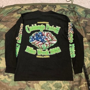 May include: Black long-sleeve shirt with a graphic on the back. The graphic features a cabbage-like design with the American flag in the center, and the text "Cabbage Patch Bike Week 2002, Sansista, Florida". The sleeves have the text "Cabbage Patch".