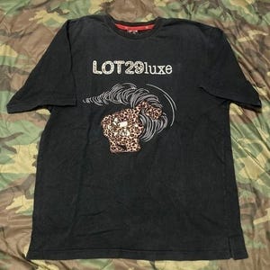 Può includere: T-shirt nero con la scritta bianca "LOT29luxe" e una grafica di una creatura con stampa leopardata con linee bianche. La maglietta ha maniche corte e girocollo.
