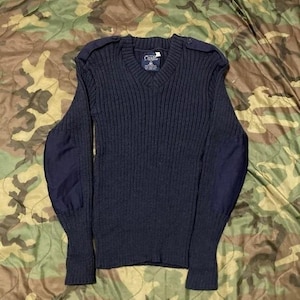 Puede incluir: Jersey azul marino con cuello en V y textura de punto acanalado. Cuenta con charreteras y coderas. La etiqueta dice "Clada". Una prenda clásica y duradera, adecuada para diversas ocasiones.
