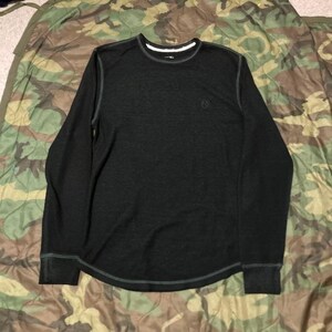 May include: Dark gray long-sleeve shirt with a crew neck and a small logo on the chest. The shirt has white trim around the neckline and cuffs, and gray stitching. The shirt is made of a soft, textured material.