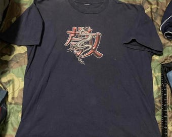 May include: Dark navy blue t-shirt with a graphic design featuring a red and white illustration of a dragon and Japanese characters. The shirt has short sleeves and a crew neck.