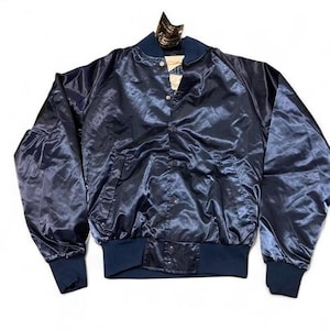 May include: Navy blue satin bomber jacket with a snap-front closure, ribbed cuffs, and a collar. The jacket has a shiny, reflective surface and two front pockets. A tag is attached to the collar.