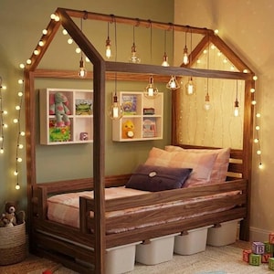 Pode incluir: Uma estrutura de cama de madeira em forma de casa com acabamento castanho escuro, apresentando lâmpadas suspensas estilo Edison e um fio de pequenas luzes redondas. A cama inclui um colchão com manta xadrez e quatro caixas de armazenamento.