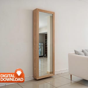 Può includere: Uno specchio alto e rettangolare con una cornice in legno chiaro è montato su una parete bianca. Lo specchio riflette una stanza con un frigorifero e scaffali. La cornice ha una venatura naturale del legno. Un divano bianco con cuscini grigi è sullo sfondo.