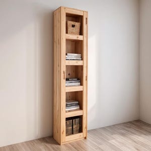 May include: A tall, light-colored wooden cabinet with glass-paned doors and multiple shelves. The shelves hold books and small woven baskets. The cabinet is made of natural wood and stands against a neutral-colored wall.