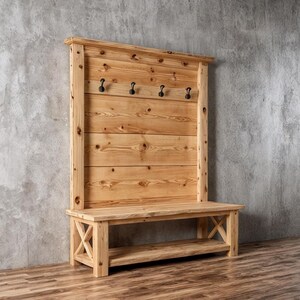 May include: Wooden hallway bench with a back panel and four black hooks. The bench has a lower shelf and X-shaped supports. The natural wood finish highlights the grain. The bench is approximately 120 cm wide.