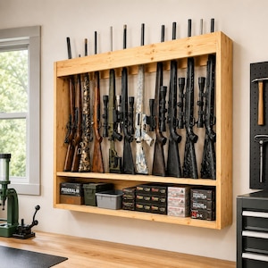 May include: A wall-mounted light wood gun rack holding ten rifles and shotguns of various styles, including black, wood-grain, and camouflage finishes. The lower shelf contains multiple boxes of ammunition and a small gray plastic storage bin.