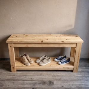 以下が含まれることがあります： 下段にスニーカーがいくつか置かれた、天然木製の靴ベンチ。 ベンチは明るい色の木材で作られており、シンプルな長方形のデザインです。 スニーカーはさまざまなニュートラルカラーです。