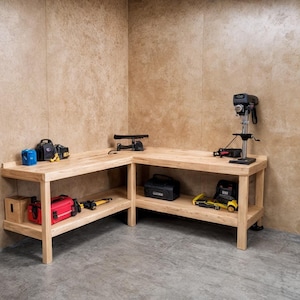 May include: A light-colored wooden workbench with an L-shape design. The workbench has a lower shelf and is filled with tools, including a drill press, power tools, and toolboxes. The workbench is in a workshop setting.