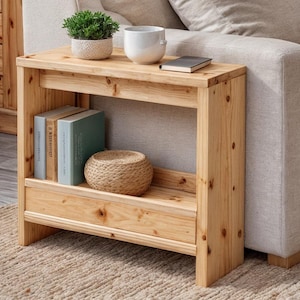 May include: A light-colored wooden side table with a shelf, holding books and a woven basket. A small potted plant and a white ceramic cup sit on top. The table is next to a beige sofa.