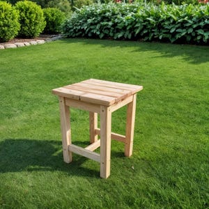 May include: A small, square wooden side table with a natural finish. The table has four legs and a slatted top. The table is approximately 18 inches tall and 16 inches wide. It is set on a green lawn.