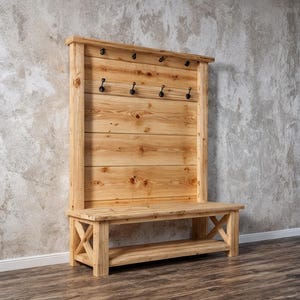 May include: A wooden hall bench with a back panel fitted with black hooks for coats or bags. The bench has a lower shelf and is made from light-coloured wood, displaying the natural grain. The bench is approximately 150 cm in length.