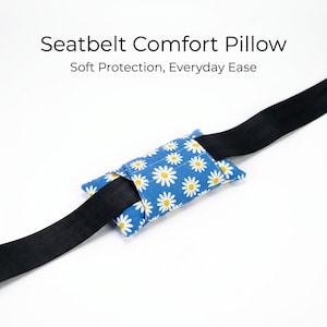 May include: A blue seatbelt comfort pillow featuring a white and yellow daisy pattern, wrapped around a black seatbelt strap. The text Seatbelt Comfort Pillow and Soft Protection, Everyday Ease is printed above the pillow on a white background.