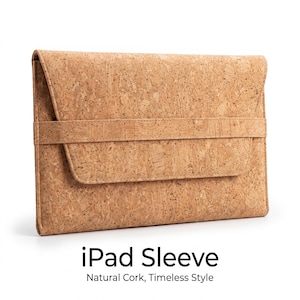 Könnte beinhalten: Eine rechteckige iPad-Hülle aus naturfarbenem Kork mit einer Umschlagklappe, die durch ein horizontales Korkband gesichert ist. Der Text "iPad Sleeve" und "Natural Cork, Timeless Style" ist unter der Hülle in Schwarz aufgedruckt.