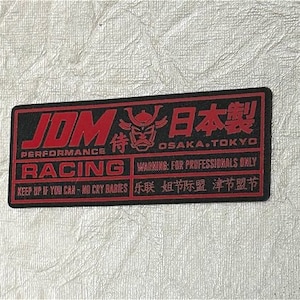 Könnte beinhalten: Ein schwarzer und roter Aufkleber mit dem Text "JOM PERFORMANCE RACING" und "日本製 OSAKA.TOKYO". Der Aufkleber enthält auch eine Warnung mit dem Text "WARNING: FOR PROFESSIONALS ONLY" und den Text "KEEP UP IF YOU CAN - NO CRY BABIES 乐联姐节际盟 津节盟节".