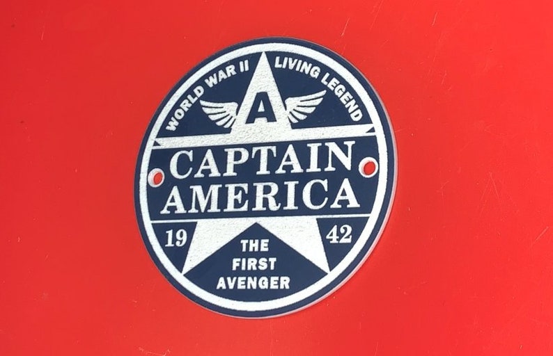 Pu&ograve; includere: Un adesivo circolare blu e bianco con una stella al centro. La stella ha il testo "Captain America" in lettere bianche. L'adesivo ha anche il testo "World War II" e "Living Legend" attorno alla stella. Il testo "The First Avenger" &egrave; nella parte inferiore della stella.