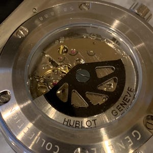 May include: Close-up of the back of a Hublot watch, showcasing the intricate internal mechanisms. The watch features a transparent window revealing the gears, jewels, and rotor. The words "Hublot" and "Geneve" are visible on the watch.