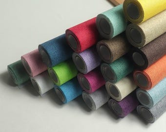 May include: A collection of rolled fabric in various colors, including red, blue, green, and yellow. The rolls are stacked, showcasing the different hues and textures of the material. The fabric appears to be a textured weave.