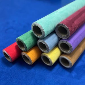 Può includere: Una collezione di carta arrotolata e strutturata in vari colori, tra cui rosso, verde, giallo e viola. I rotoli sono disposti diagonalmente, mostrando le diverse tonalità e trame del materiale. Lo sfondo è blu.