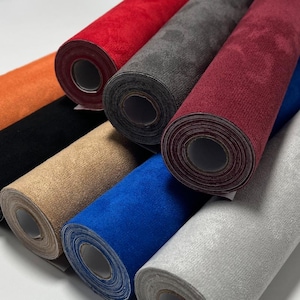 May include: A collection of rolled fabric in various colors, including red, orange, black, tan, blue, gray, and burgundy. The rolls are arranged in a diagonal pattern, showcasing the different textures and hues of the material. The fabric appears to be a soft, suede-like material.