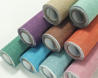 May include: A collection of rolled-up wallpaper samples in various colors, including purple, brown, orange, and pink. The wallpaper has a textured, woven appearance, suggesting a linen or fabric-like material. The rolls are arranged diagonally, showcasing the different colors.