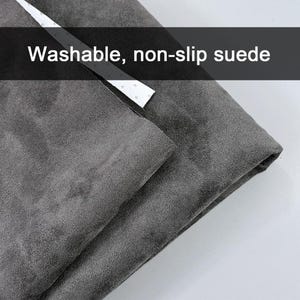 Puede incluir: Un trozo de tela de ante gris oscuro con una textura suave y mate. Se observa una tira blanca con pequeños puntos espaciados uniformemente a lo largo del borde. El texto "Washable, non-slip suede" está superpuesto en la imagen, describiendo las características.