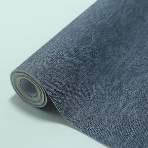 May include: A roll of denim-textured wallpaper. The wallpaper is a dark blue color with a subtle, woven pattern. The roll is partially unrolled, revealing the paper's texture and the white backing.