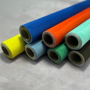 May include: A collection of rolled-up, textured paper in various colors, including blue, orange, yellow, light blue, green, and brown. The rolls are arranged diagonally, showcasing the different hues and textures of the material.