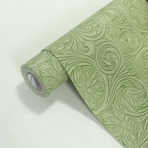 以下が含まれることがあります： 緑色の壁紙のロールで、エンボス加工された花の模様です。このパターンは、様式化された花と渦巻く葉を特徴とし、テクスチャ加工された装飾的な表面を作り出しています。紙は明るく落ち着いた緑色です。