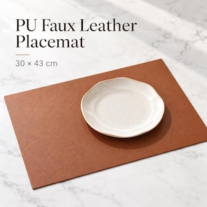 May include: A rectangular brown PU faux leather placemat measuring 30 x 43 cm, featuring a textured surface. A white, round, slightly wavy-edged plate is centred on the mat. The text PU Faux Leather Placemat 30 x 43 cm is visible.