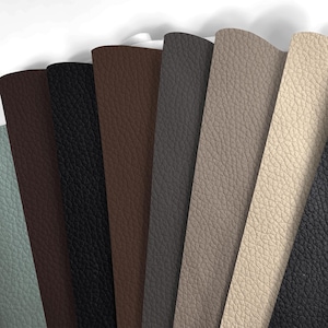 May include: A fan of various leather swatches in shades of gray, brown, and black. The swatches have a textured surface and are arranged in a semi-circular pattern. The colors range from light beige to dark charcoal.