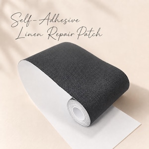 May include: A roll of dark charcoal grey self-adhesive linen repair patch material with a visible woven fabric texture. The roll is partially unspooled, revealing a white backing paper. The text Self-Adhesive Linen Repair Patch is visible.