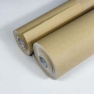 May include: Two rolls of brown craft paper are shown against a white backdrop. The paper is tightly rolled, revealing the layered edges. The paper appears unused, suitable for crafting or packaging. Each roll is approximately 30 cm in diameter.