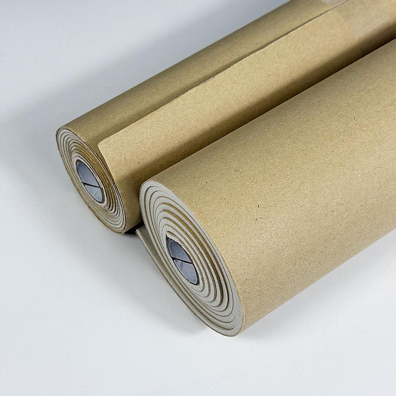 May include: Two rolls of brown craft paper are shown against a white backdrop. The paper is tightly rolled, revealing the layered edges. The paper appears unused, suitable for crafting or packaging. Each roll is approximately 30 cm in diameter.