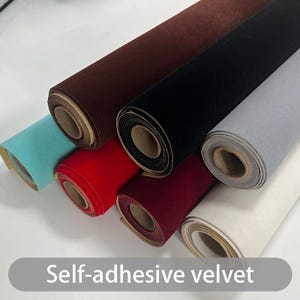 May include: Rolls of self-adhesive velvet in various colors, including brown, black, gray, red, and teal. The rolls are tightly wound, showing the texture of the velvet material. The text "Self-adhesive velvet" is visible at the bottom.