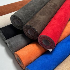 Peut inclure: Plusieurs rouleaux de tissu de différentes couleurs, dont rouge, orange, bleu, marron et gris. Les rouleaux sont bien enroulés, mettant en valeur la texture et les variations de couleur du matériau. Le tissu semble être un matériau doux, semblable à du daim.