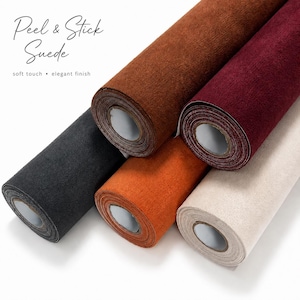 Op de afbeelding: Vijf rollen zelfklevende suèdestof in zwart, bruin, bordeaux, oranje en crème. De tekst Peel & Stick Suede soft touch elegant finish is zichtbaar. Elke rol heeft een gestructureerd oppervlak en een centrale kartonnen kern.