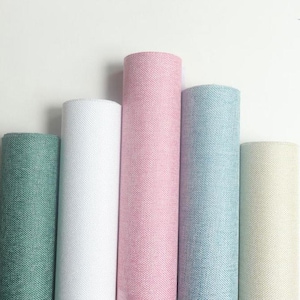 May include: Five rolls of fabric in shades of green, white, pink, blue, and cream. The fabric has a textured weave. The rolls are arranged vertically against a white background.